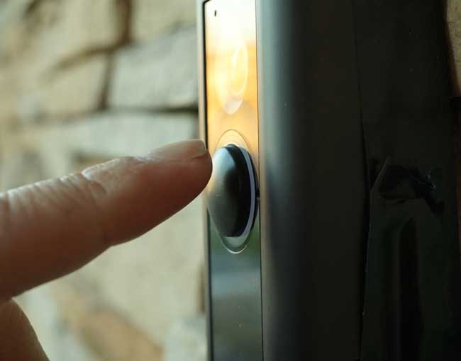 A finger about to push the button on a doorbell video camera