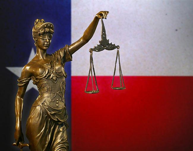 A statue of Lady Justice in front of the Texas flag
