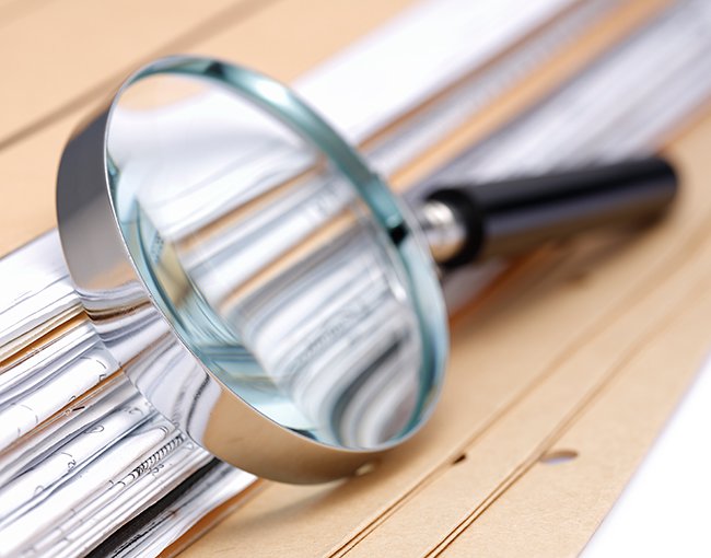 magnifying glass rests on a stack of documents